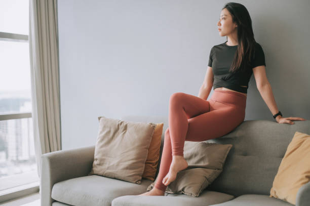 asian chinese beautiful female with yoga clothing sitting on sofa posing in living room  asian yoga pants stock pictures, royalty-free photos & images