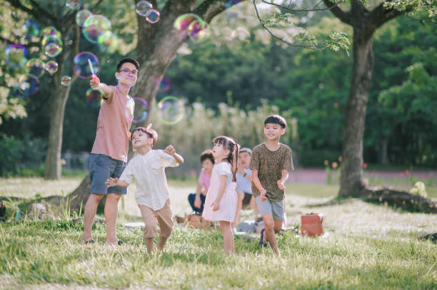 asian chinese father playing with his children with bubble wand at public park in the morning backlit sunlight asian chinese father playing with his children with bubble wand at public park in the morning backlit sunlight self-care stock pictures, royalty-free photos & images