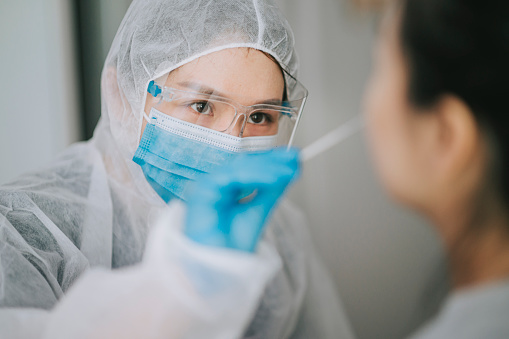 rapid diagnostic test asian chinese female doctor with PPE taking mouth swab from patient Coronavirus test. Medical worker in protective suite taking a swab for corona virus test, potentially infected woman