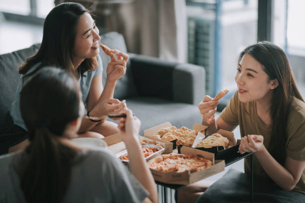 3 asian chinese female friends having pizza for lunch in their living room bonding time 3 asian chinese female friends having pizza for lunch in their living room asian family eating together stock pictures, royalty-free photos & images