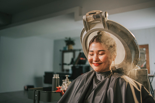 Asian chinese female getting her hair steaming and moisturizing treatment in hair salon