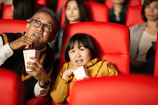 Asian Chinese grandfather and granddaughter together with group of audience watching movie in cinema enjoying the show excitement
