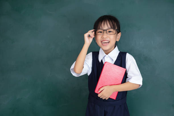 Asian Chinese little Girl in uniform standing against green blackboard stock photo
