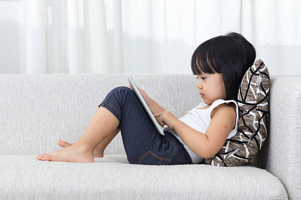 Asian Chinese little girl lying on the sofa with tablet stock photo