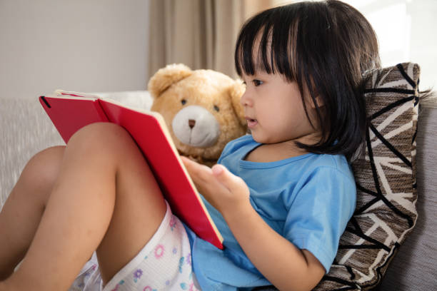 Asian Chinese little girl reading book with teddy bear stock photo