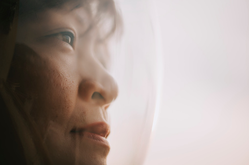 Asian chinese mid adult female astronaut looking at earth sunrise through window from spaceship at outer space