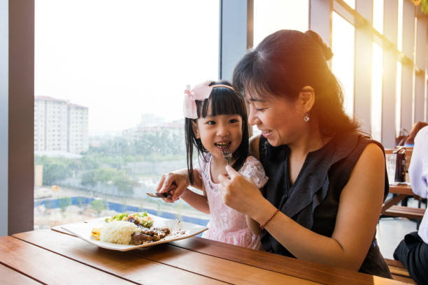 Asian Chinese mother and daughter eating steak Asian Chinese mother and daughter eating steak in the restaurant. asian family eating together stock pictures, royalty-free photos & images