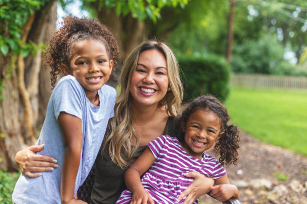 asian chinese mother with two daughters of mixed chinese and african american ethnicity in a green lush back yard setting posing for portraits smiling and being silly - foster kids imagens e fotografias de stock