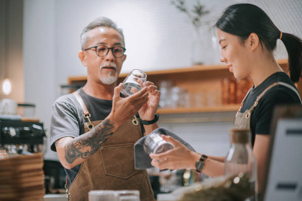 asian chinese senior male cafe owner and daughter inspecting cleanliness of drinking glass at bar counter table getting ready to coffee shop opening - saki baba stok fotoğraflar ve resimler