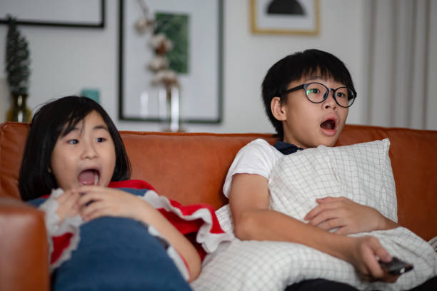 Asian Chinese sibling watching scary movie on television together at their home Asian Chinese sibling watching scary movie on television together at their home asian kids watching tv stock pictures, royalty-free photos & images