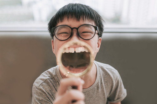 asian chinese teenage boy Smile zoom tooth care holding magnifying glass on his teeth looking at camera humor