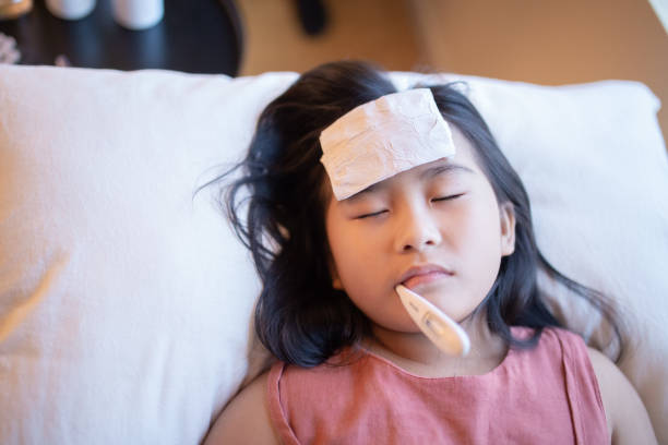 Asian Chinese young girl sick lying on the bed with thermometer in her mouth.  flu stock pictures, royalty-free photos & images