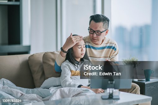 istock asian chinesse father taking temperature for his sick daughter on sofa living room videocall with his doctor via digital tablet 1309783324