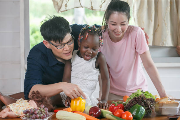 Asian couple cooking and tasting food with african american girl together in kitchen at  home . stock photo