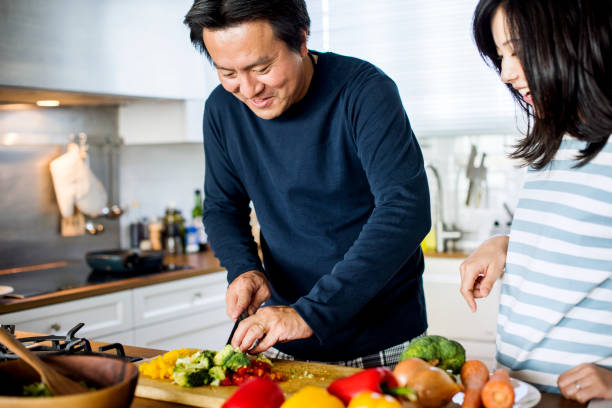 asian couple cooking in the kitchen - woman chopping vegetables imagens e fotografias de stock