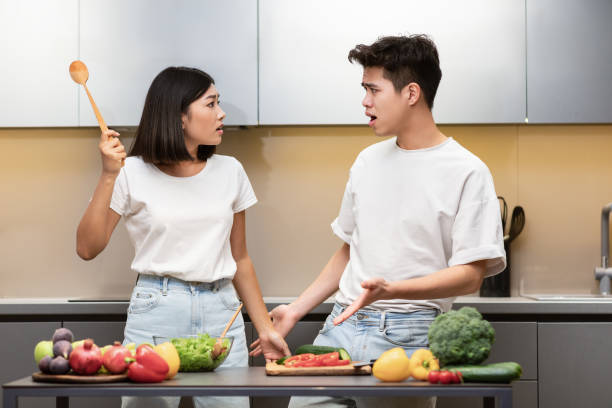 Asian Couple Having Quarrel Cooking Standing In Kitchen At Home Asian Couple Having Quarrel Cooking Standing In Kitchen At Home. Unhappy Wife Threatening Husband Raising Spoon, Cooking Dinner Together. Married Life Conflicts And Relationship Problems disgust photos stock pictures, royalty-free photos & images