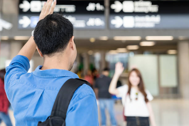 Asian couple say Hi or goodbye for abroad at airport. Back asian man waving hand goodbye girlfriend. Travel ,airport terminal concept.  wave goodbye asian stock pictures, royalty-free photos & images