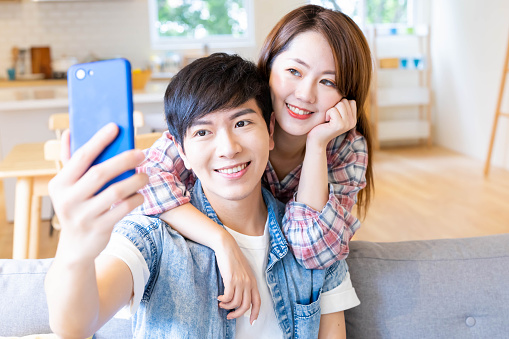Smiling asian young couple take selfie in the living room at home