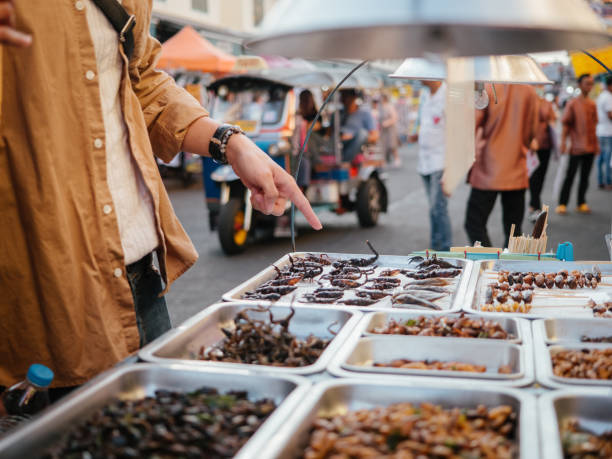 Asian couple tourists buying fired insects at street food. Young couple tourists buy fired insects in a street food marketplace in Bangkok, at Khao San Road arthropod stock pictures, royalty-free photos & images
