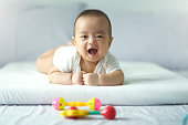 istock Asian cute baby in white sunny bedroom. Newborn child relaxing on bed. Nursery for young children. Textile and bedding for kid. Family morning at home. New born kid during tummy time with toy. 1297217179