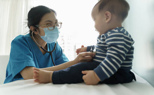 Asian Doctor wearing protective face mask examining baby. stock photo