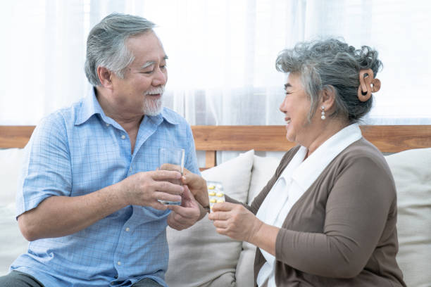 Asian elderly couple, Taking care of health in retirement, Senior woman helping her husband take a pills or vitamin pills at home. stock photo