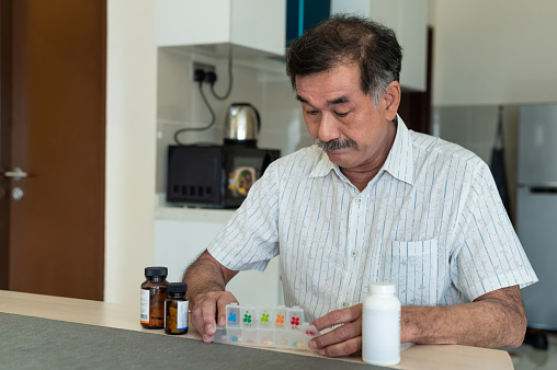 Senior man sort his weekly prescription medication at dining table in the morning. Home Medical & Healthcare, Telehealth & Telemedicine, Stay at Home Concepts.