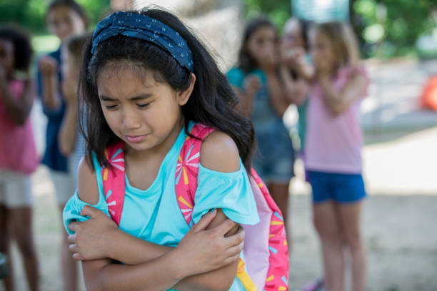 Asian elementary age little girl cries while being teased at school Elementary age Asian little girl is crying outside of school on playground. Diverse classmates are teasing and bullying her. philippines girl stock pictures, royalty-free photos & images