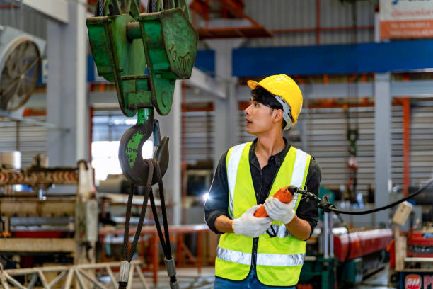 Asian engineer worker is using overhead crane hoist to carry raw materials inside metal sheet manufacturing factory for heavy industrial concept stock photo
