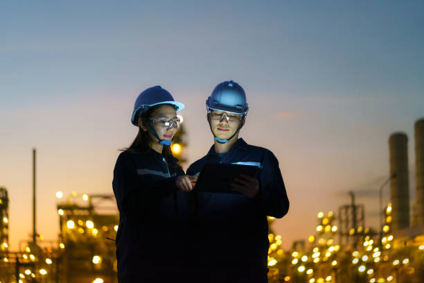 Asian engineers, man and woman are checking the maintenance of the oil refinery factory at night via digital tablets. stock photo