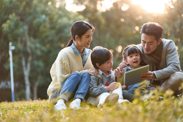 asian family with two children relaxing outdoors in park stock photo