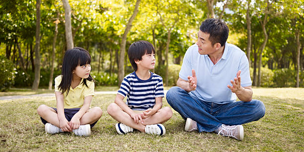 asian father and children talking in park asian father and two children sitting on grass having an interesting conversation, outdoors in a park. child korea little girls korean ethnicity stock pictures, royalty-free photos & images