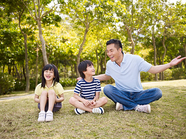 asian father and children talking in park asian father and two children sitting on grass having an interesting conversation, outdoors in a park. child korea little girls korean ethnicity stock pictures, royalty-free photos & images