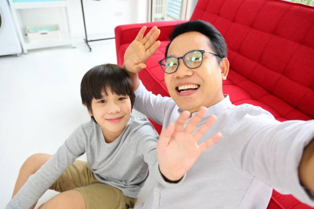 Asian father and son waving hand to camera for video call for online and internet communication Asian father and son waving hand to camera for video call for online and internet communication concept wave goodbye asian stock pictures, royalty-free photos & images
