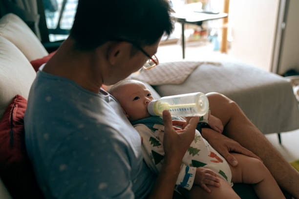 ソファで彼の幼児の娘を養うアジアの父親のボトル - 乳育児 ストックフォトと画像