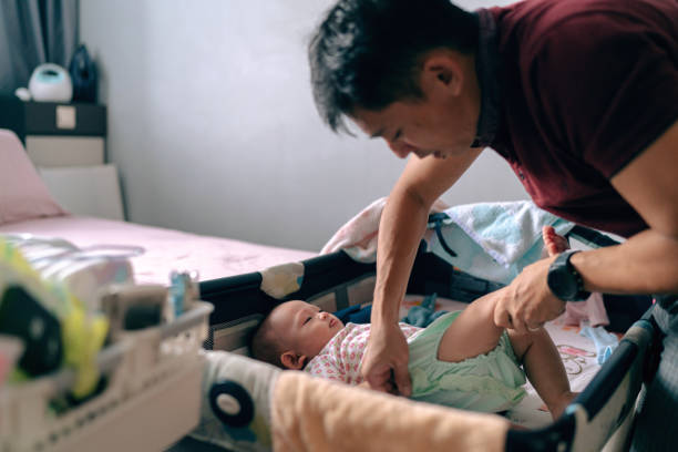 Asian father enjoys the time spent with his baby girl during diaper changing stock photo