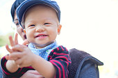 アジアの父は幸せな幼児赤ちゃん少年笑顔の身に着けているセーター、よだれかけ、帽子、屋外の庭で手をたたく