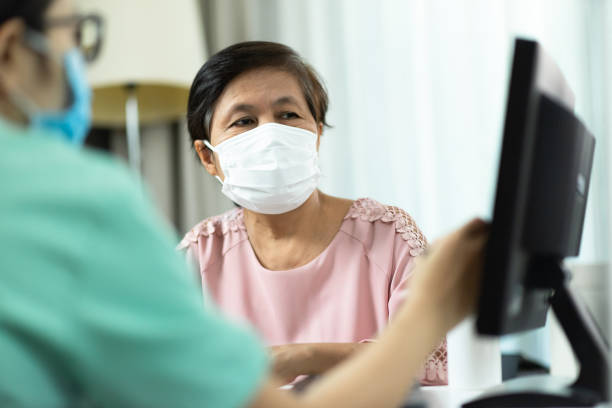 asiatiska kvinnliga läkare eller sjuksköterska i grön uniform talar ge råd till äldre kvinna patient i rosa tyg och ser till datorskärmen - patient bildbanksfoton och bilder