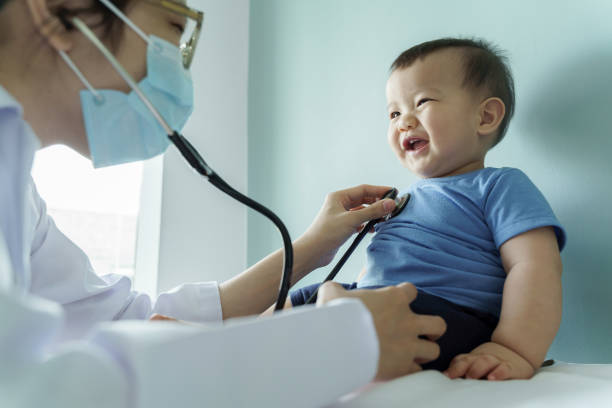 Asian female Pediatrician doctor examining little cute smiling Baby boy with stethoscope in medical room stock photo