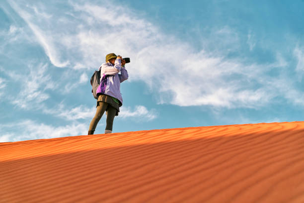 asian female photographer walking on top of sand dune stock photo