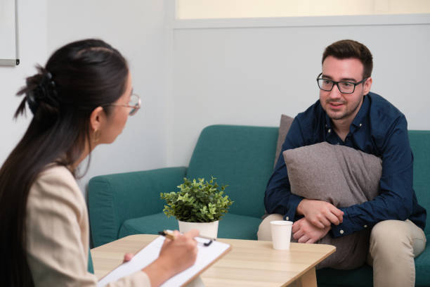 Asian female psychologist and caucasian man patient at therapy. stock photo