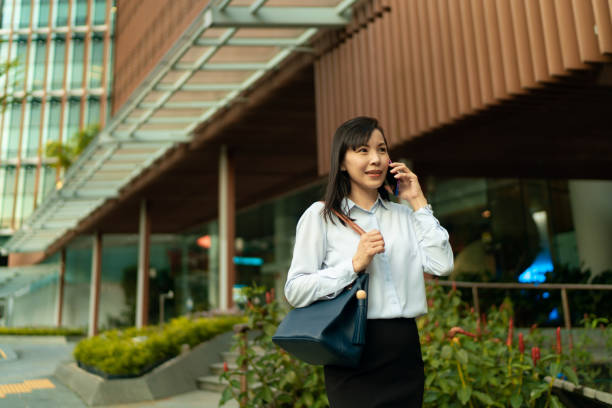 Asian female using mobile phone against city backdrop Asian female using mobile phone against city backdrop Smart Skirt for women stock pictures, royalty-free photos & images