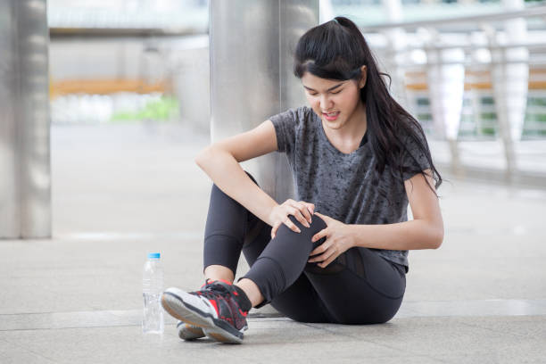 asian fitness young woman  Running injury leg accident  of workout exercising on street in urban city . sport runner girl sitting on floor holding knee in  pain stock photo