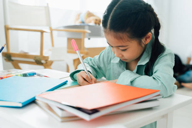 Asian girl doing homework Chinese girl sitting at table writing in school book child doing homework asian stock pictures, royalty-free photos & images