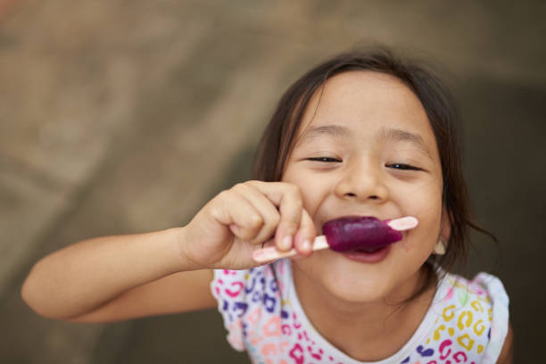 Asian girl eating ice cream in outdoor Asian girl eating ice cream in outdoor. Filipina kid eating an ice cream and staring at camera. filipino family stock pictures, royalty-free photos & images