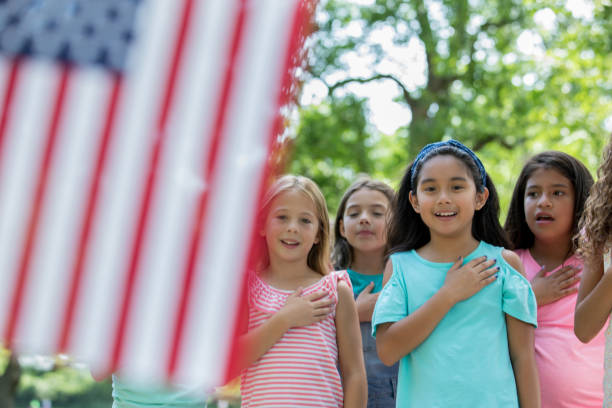 Asian girl recites Pledge of Allegience to American flag with friends stock photo
