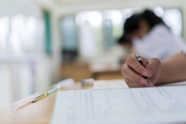 Asian Girl Student in exam test school, Side View of high school or university holding writing document paper answer sheet and lecture final exams in classroom with white uniform pupil of Thailand stock photo