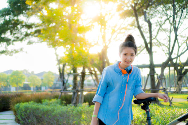Asian girls Happy standing by the bike. Orange headphones. Sunset time stock photo