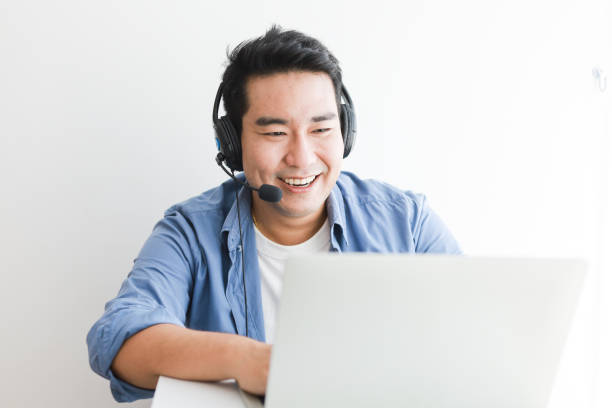 Asian handsome man in blue shirt using laptop with headphone talking smile and happy face stock photo