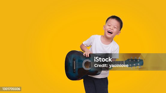 istock Asian happy smiling boy having fun playing guitar isolated on colored background, Music for kids and toddlers concept 1301705506